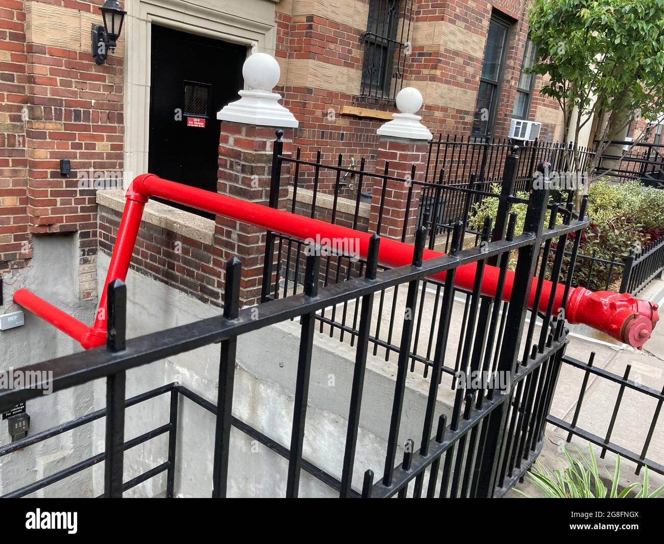 Bright red standpipe connected to the London Terrace apartment complex in Chelsea in New York on Wednesday, July 14, 2021.  A standpipe is a dry line that the fire department connects to deliver water to upper, or in this case below ground, floors.  (© Frances M. Roberts) Stock Photo