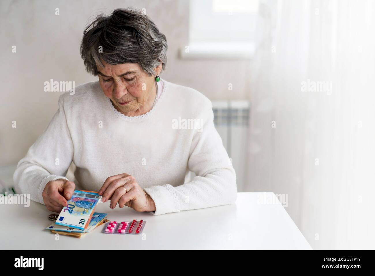 An old lady in a white sweater is planning her budget. Stock Photo