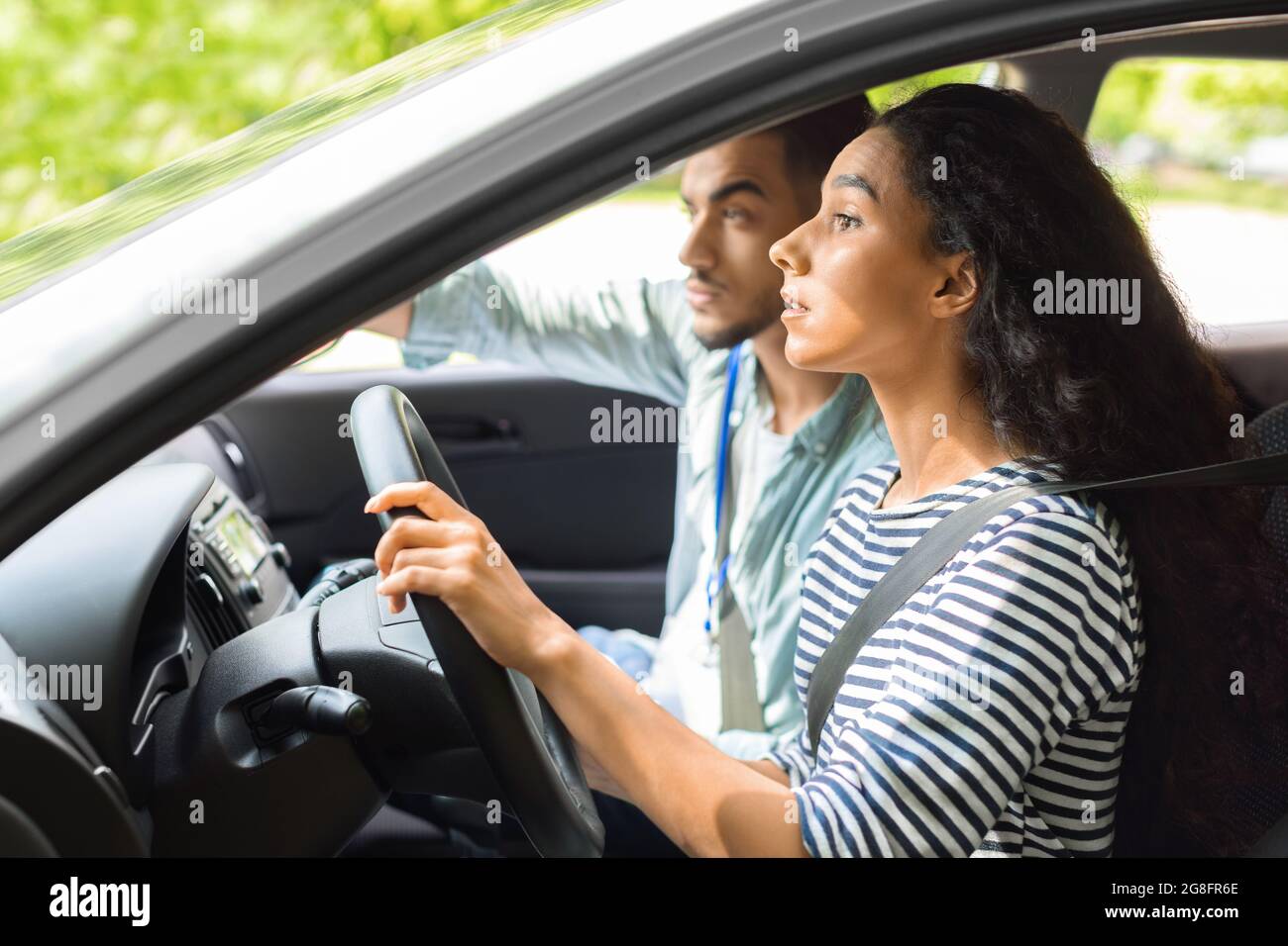 Nervous young lady driving school student driving car with instructor