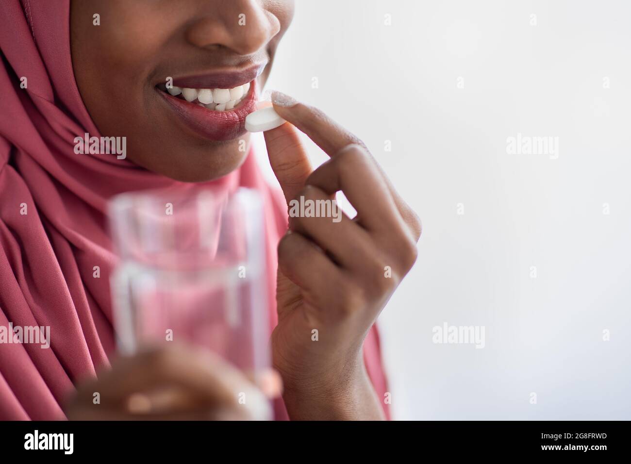 Black Muslim Woman In Hijab Holding Glass Of Water And Taking Pill Stock Photo