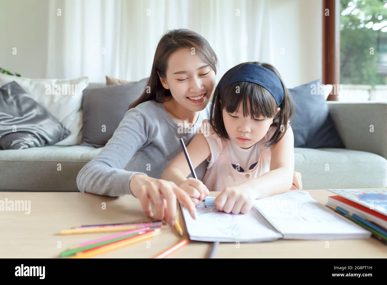Asian mother teaching her cute kid daughter to studying in living room at home Stock Photo