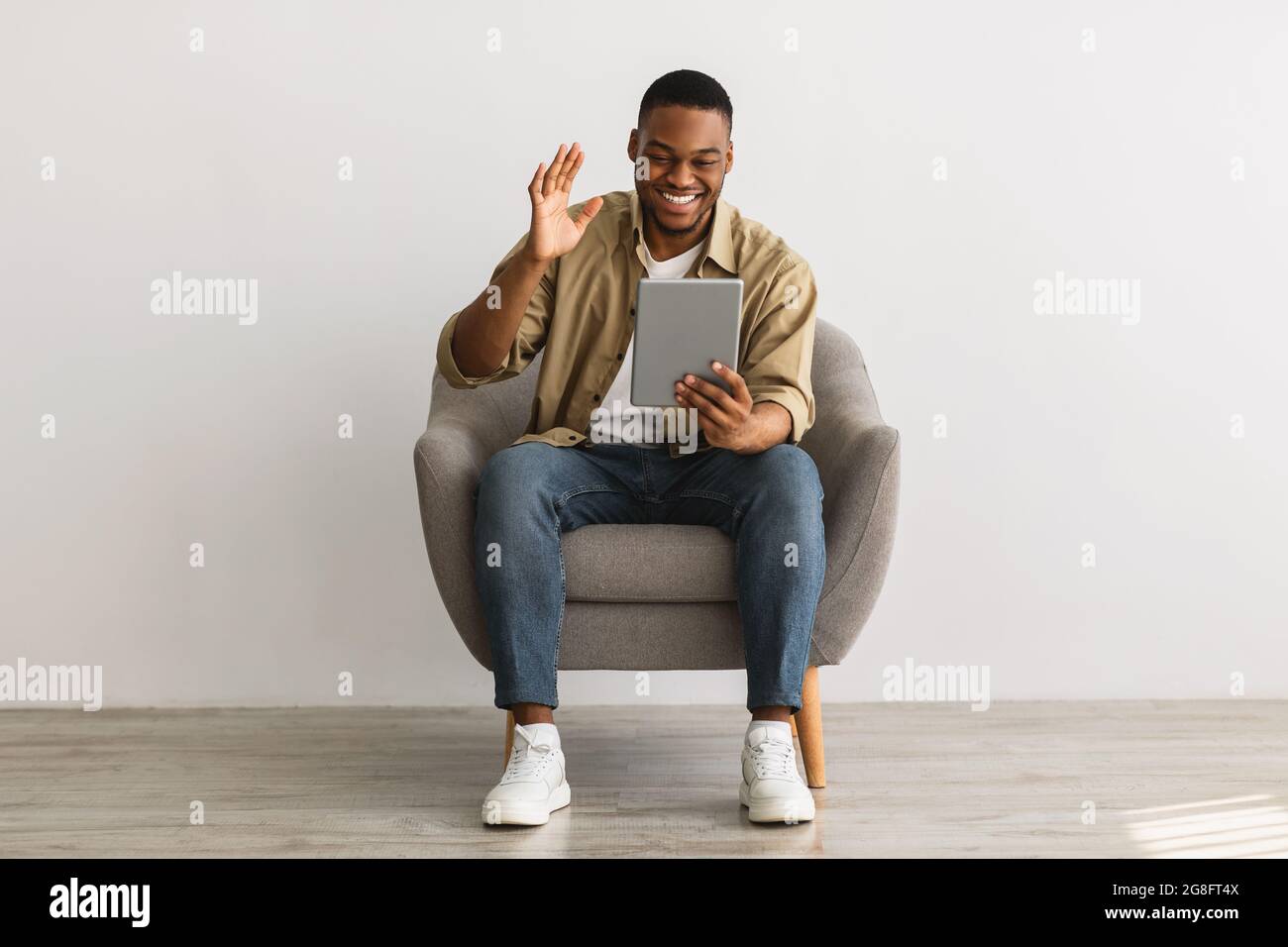 African Man Talking Video Calling Via Tablet Over Gray Wall Stock Photo