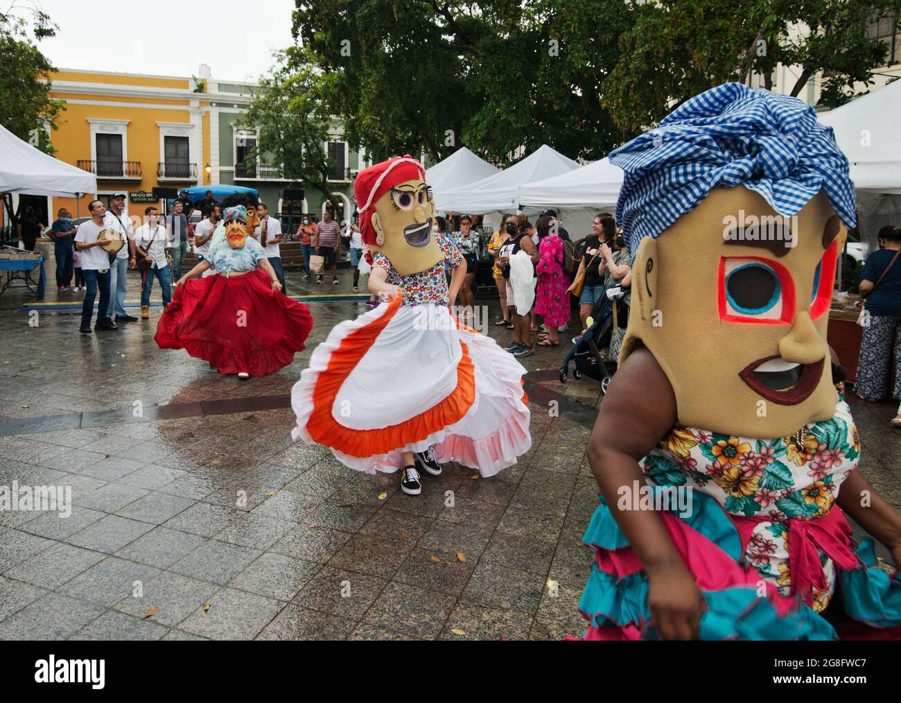 Female Cabezudos (Big Heads) dance in the De Armas Plaza after a summer rain in Old San Juan, Puerto Rico, USA. Stock Photo