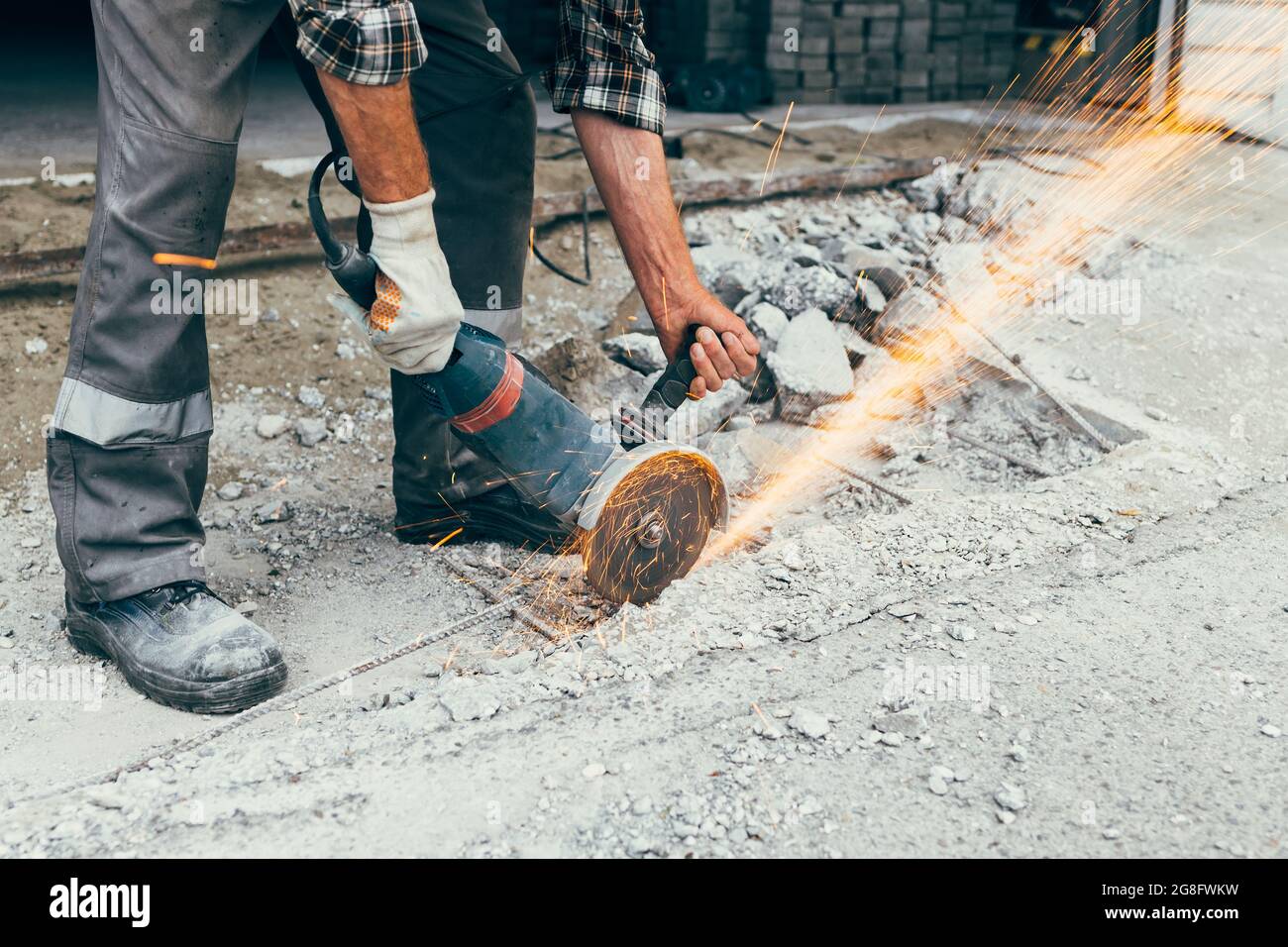 A worker with a grinder cuts the concrete pavement of the road and sparks fly. Construction and repair of the roadway. Stock Photo