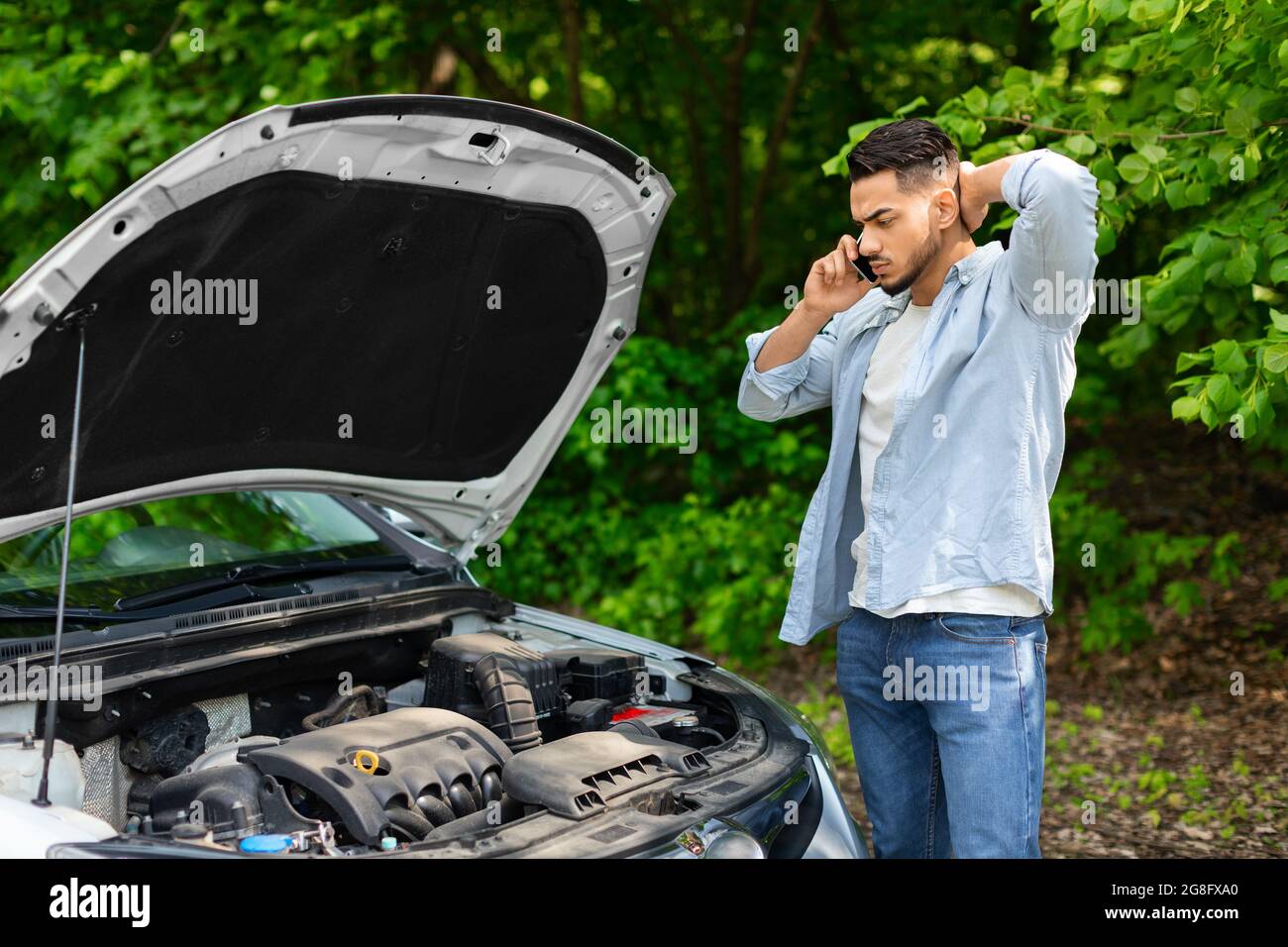 Sad arab man looking at engine and calling auto service Stock Photo