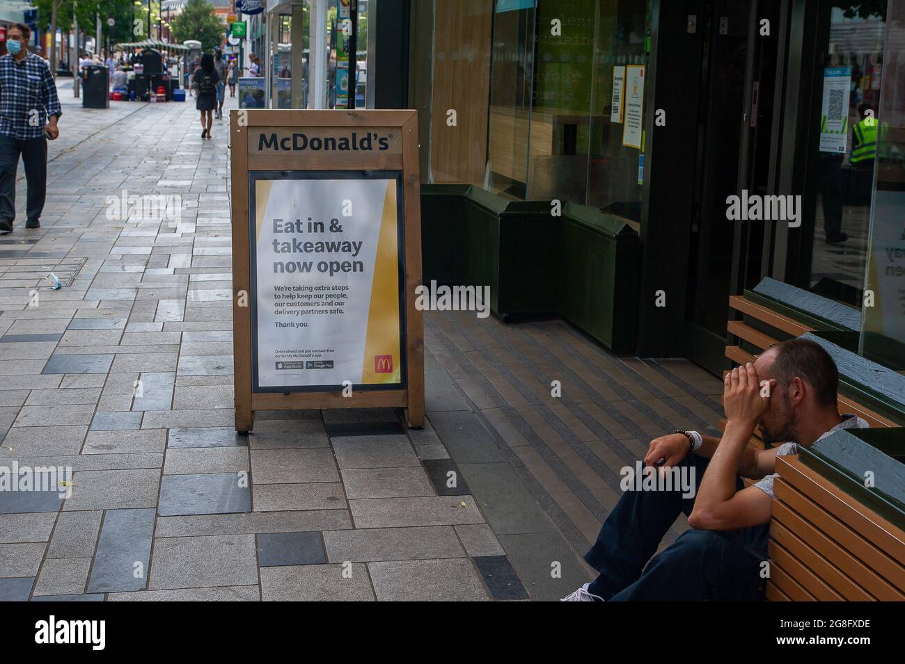 Slough, Berkshire, UK. 20th July, 2021. A man sits outside McDonald's in Slough High Street. The restaurant is now open to eat in again. Credit: Maureen McLean/Alamy Live News Stock Photo
