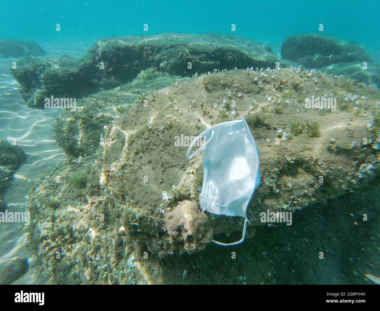 Discarded surgical face mask floating on contaminated sea ecosystem,covid19 environment pollution Stock Photo