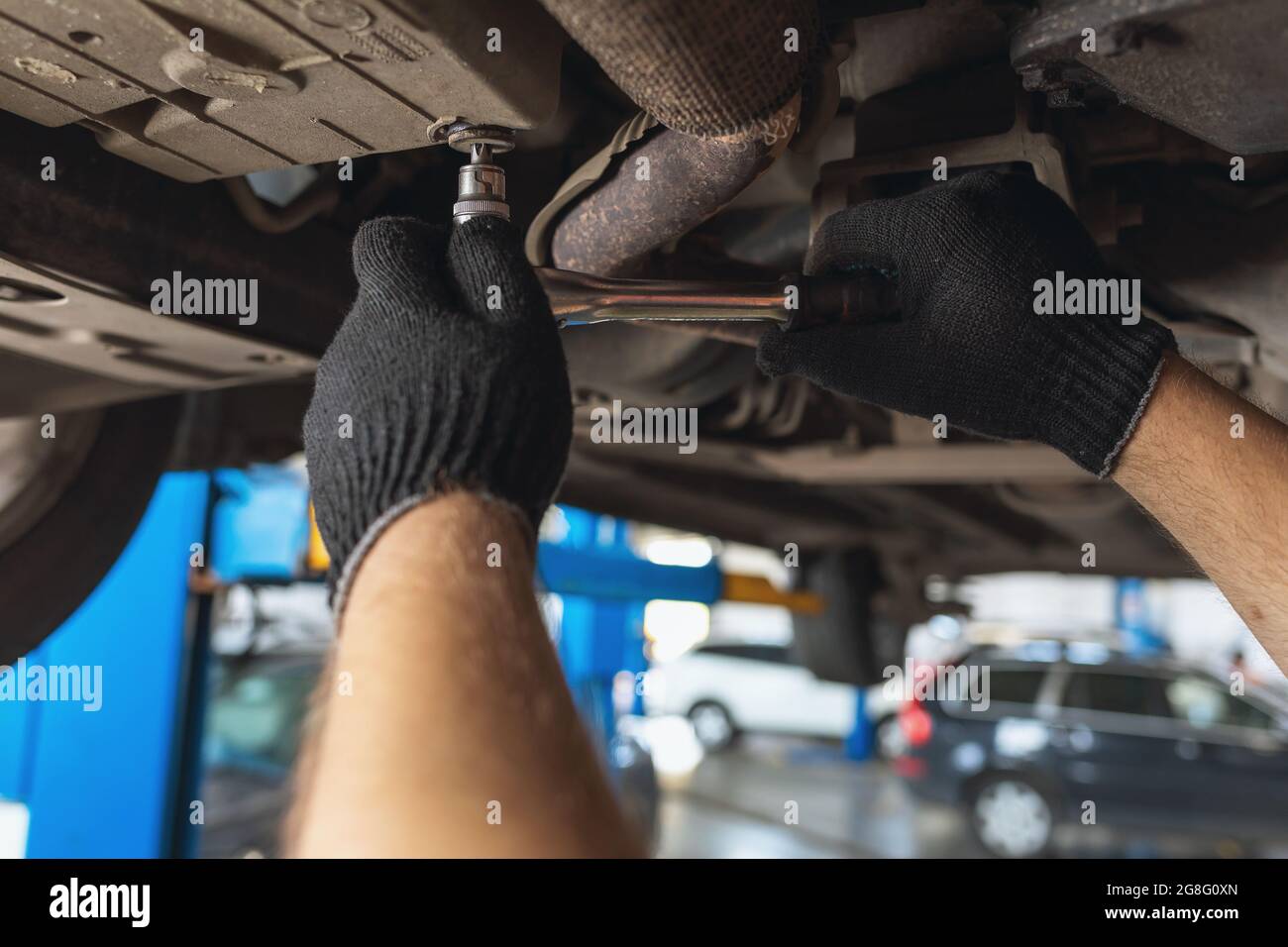 An auto mechanic unscrews the oil drain plug in the cars crankcase with a key, close-up Stock Photo