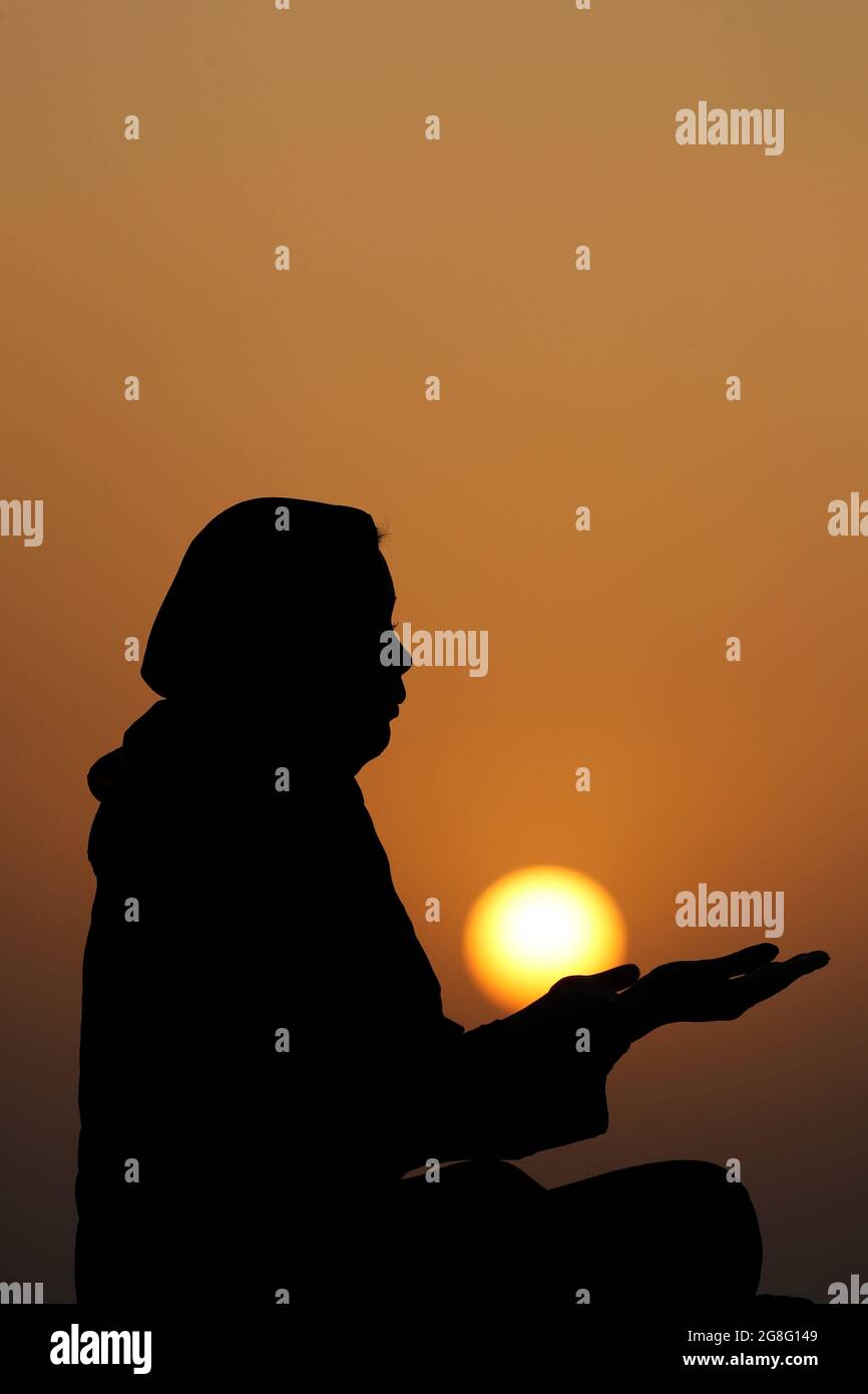 Silhouette of a Muslim woman in abaya praying with her hands at sunset, United Arab Emirates, Middle East Stock Photo