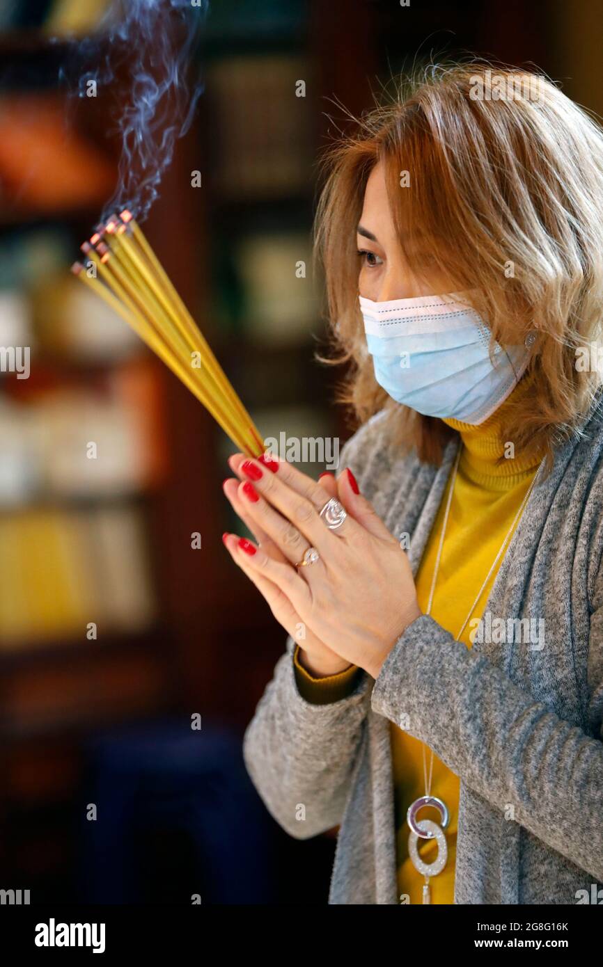 Woman wearing surgical mask praying with incense sticks, Tu An Buddhist Temple, Haute Savoie, France, Europe Stock Photo