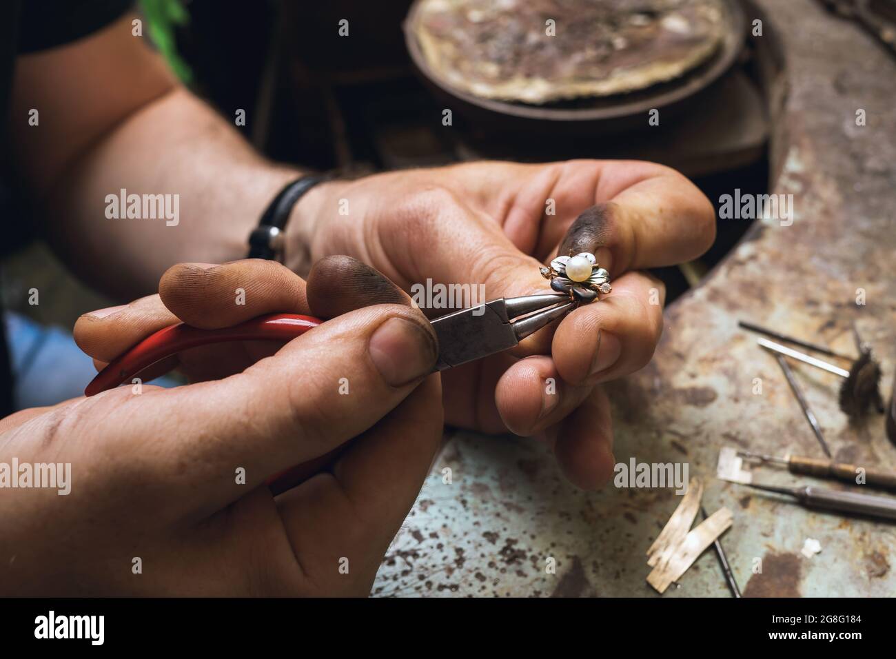 A jeweler disassembles a gold ring with pearls in a workshop, close-up Stock Photo