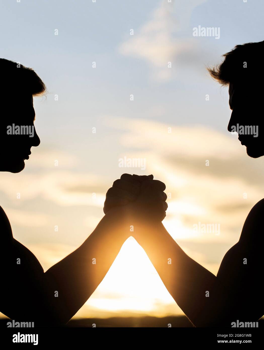 Two men arm wrestling. Rivalry, vs, challenge, strength comparison. Sunset, sunrise. Silhouette of hands that compete in strength. Rivalry, closeup of Stock Photo