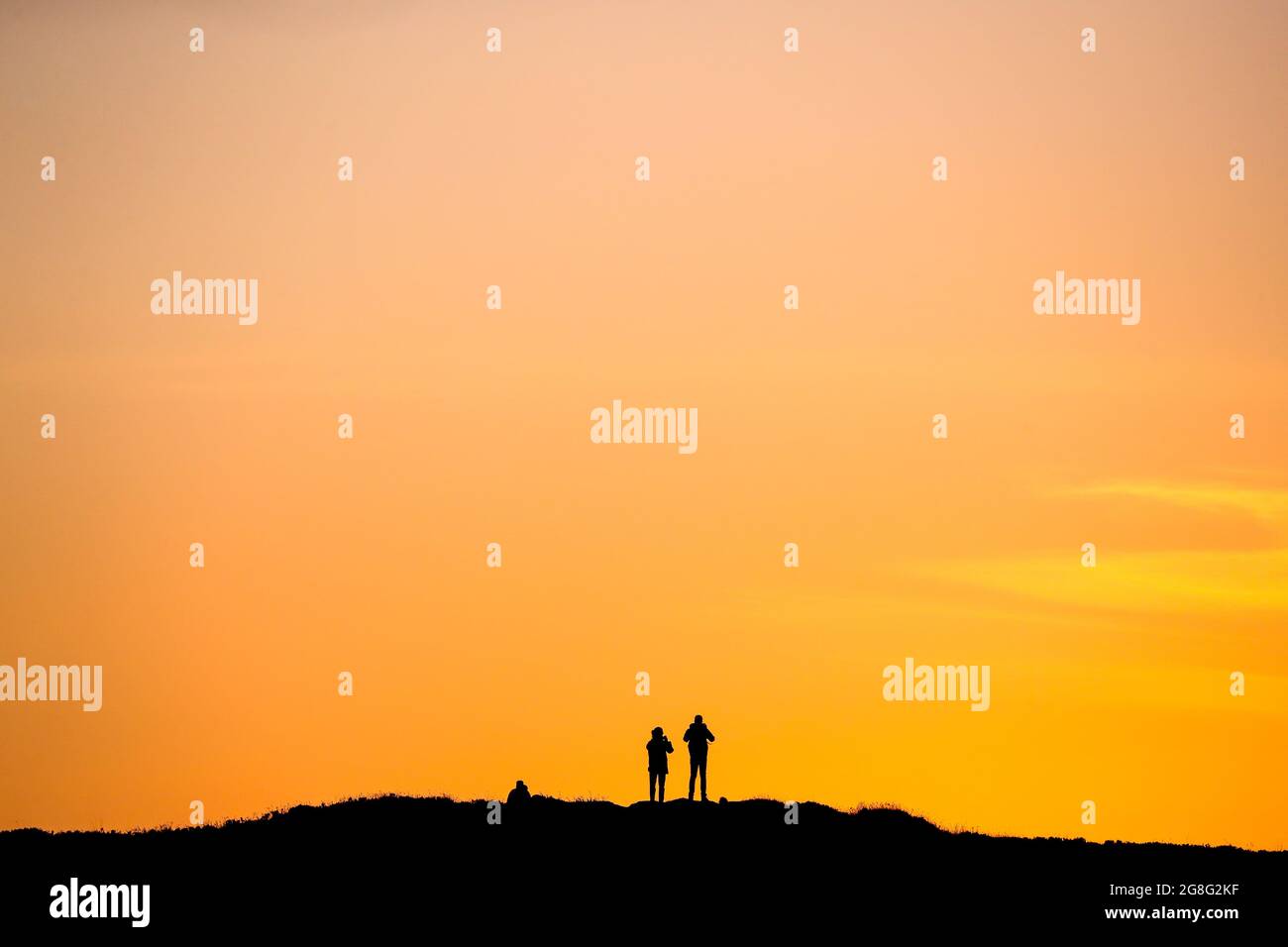 People watch the sunset on top of Cavehill mountain, overlooking Belfast in Northern Ireland, on the longest day of the year during Summer Solstice. Stock Photo