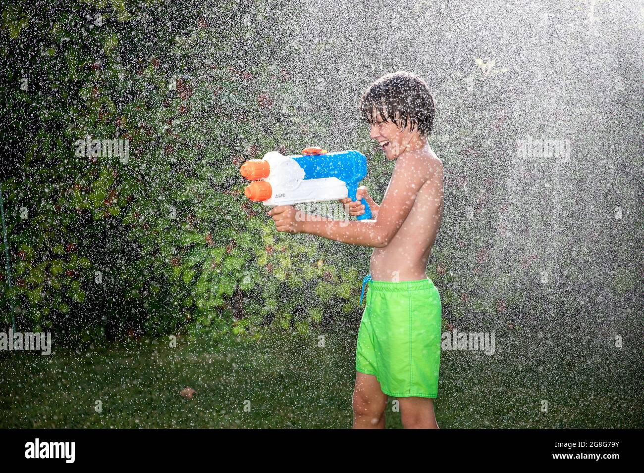 child spraying water all over on a hot summer day. Boy wearing swimming