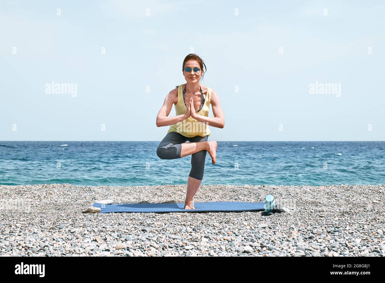 Slim Woman doing Virksasana or tree pose on the beach in the morning ...