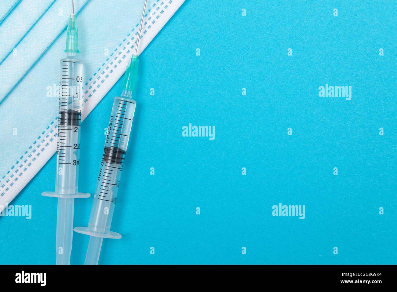 Several Syringe and Face Mask on Blue Table - Top View. Syringes are Prepared for Vaccination or Injection. Medical Experiment. Blue Disposable Medical Mask. Virus protection - Flat Lay Stock Photo