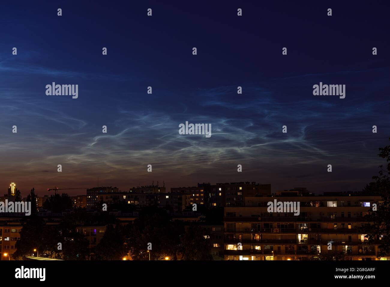 Noctilucent cloud (NLC, night clouds) over housing project and church in the evening. Cloud-like phenomena in mesosphere. They are highest clouds in E Stock Photo