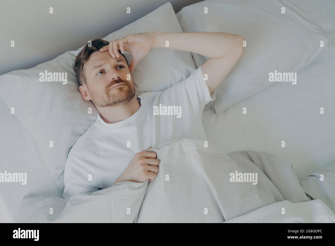 Young tired bearded man lying on bed with open eyes Stock Photo