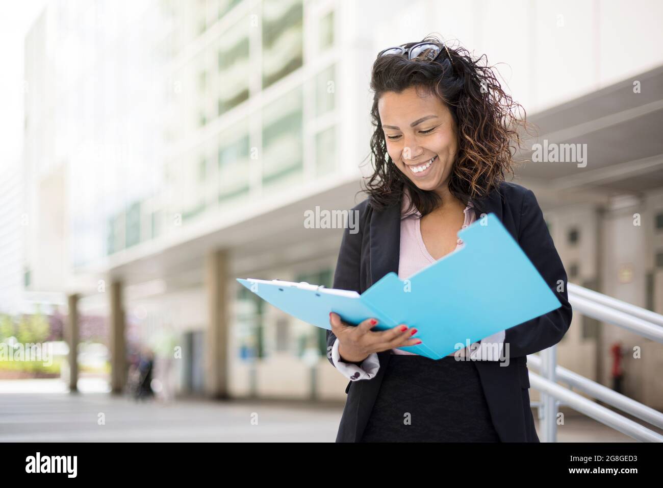 Smiling young Latin American business woman reading some documents in the street. Space for text. Stock Photo
