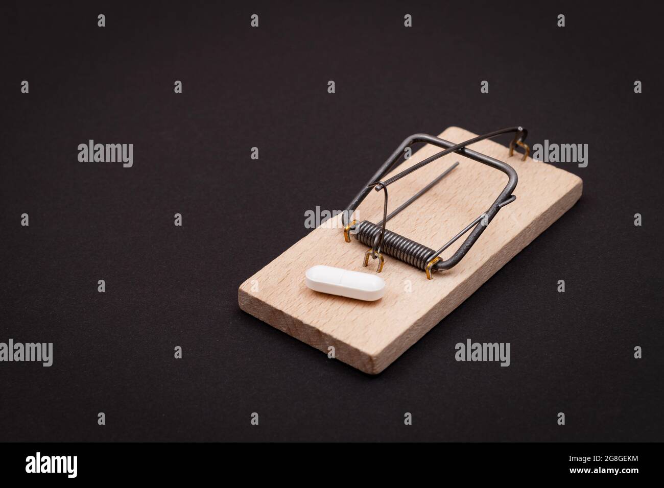 Pharmaceutical Addiction or Big Pharma Trap - White Pill in Wooden Mousetrap on Black Background Stock Photo