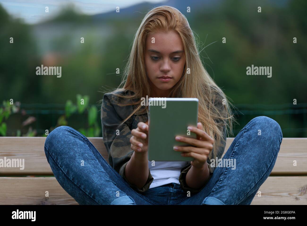 young woman sitting informally on a bench while enjoying digital content, perhaps in social networks, surfing the internet or videos Stock Photo