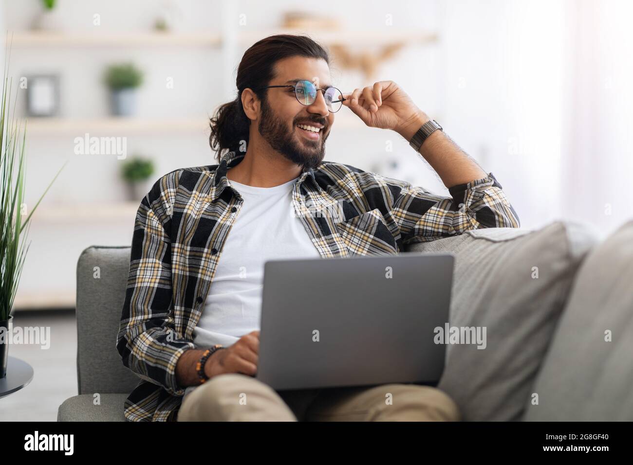 Dreamy arab guy freelancer working from home, using laptop Stock Photo