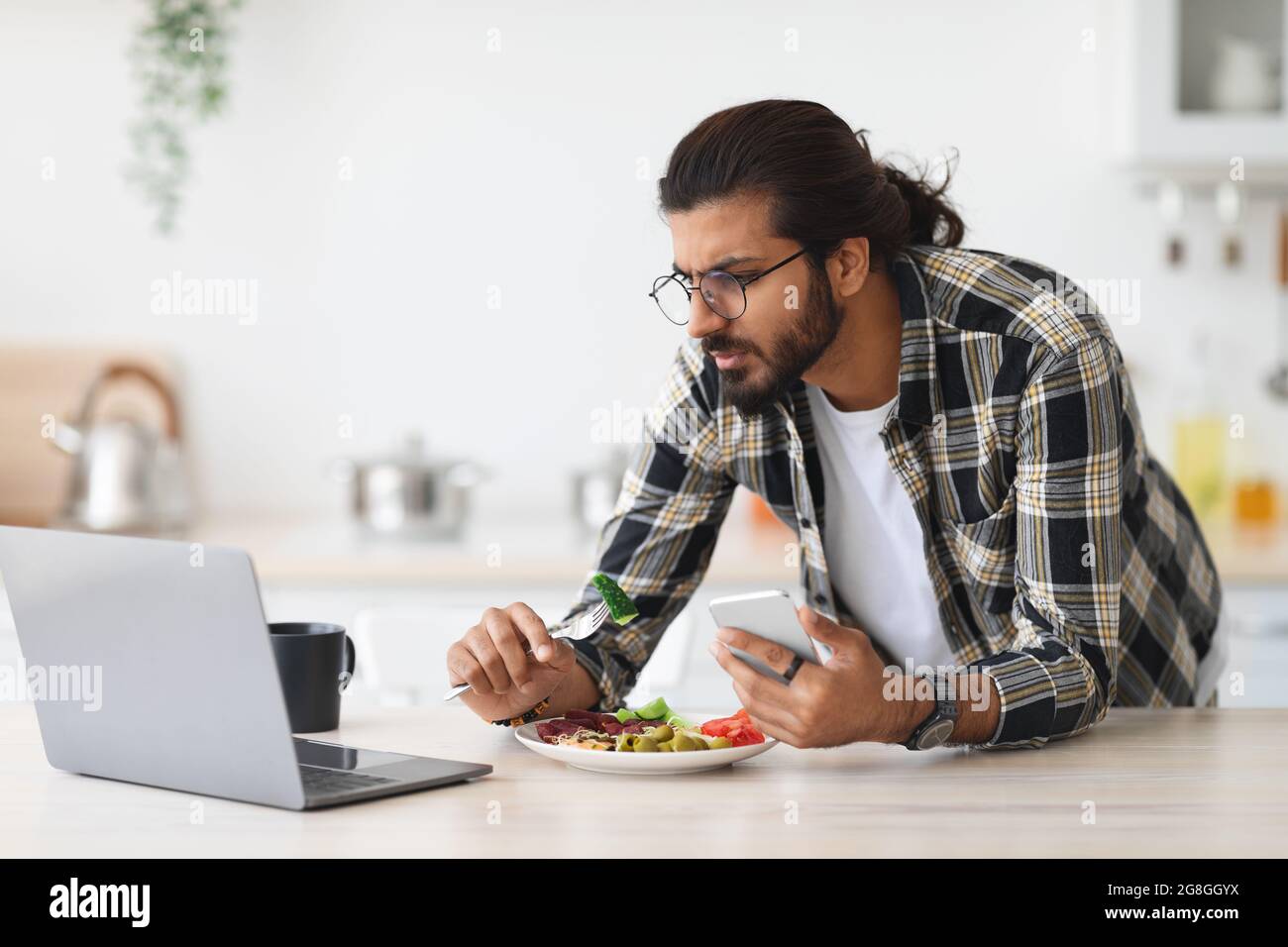 Irritated middle-eastern guy having snack while working from home Stock Photo
