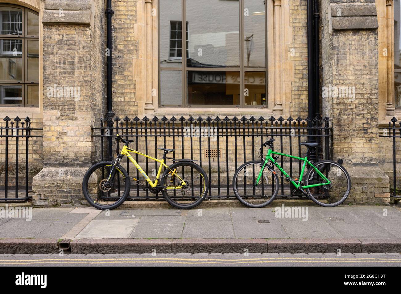 A yellow bike and a green bike locked to railings in a city centre. Stock Photo