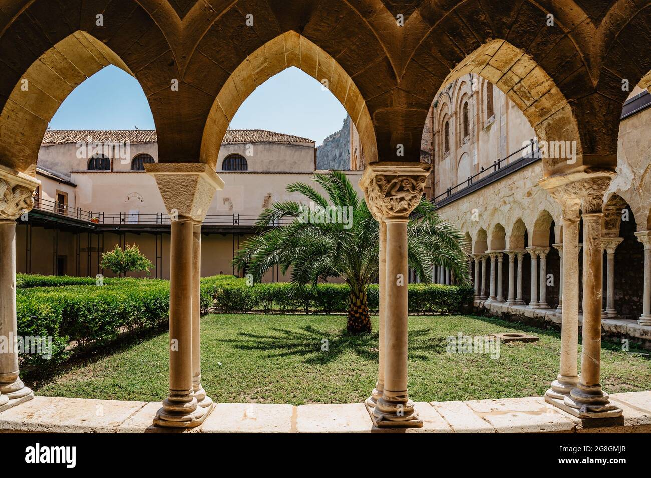 Cefalu,Sicily-June 6, 2021.Roman Catholic cathedral with cloister,arcade has pointed arches and columns.Monastery courtyard garden. Famous UNESCO Heri Stock Photo