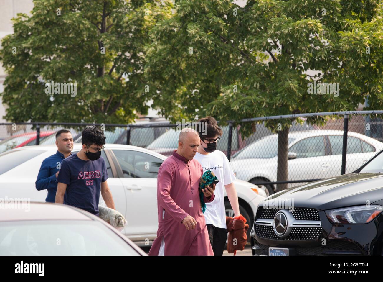 Some Muslim men are walking together through the parking lot with their prayer rugs during Eid festival. Stock Photo