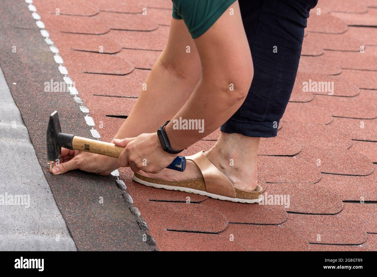 Woman laid of bitumen roof shingles. Disregard of occupational health and safety. Stock Photo