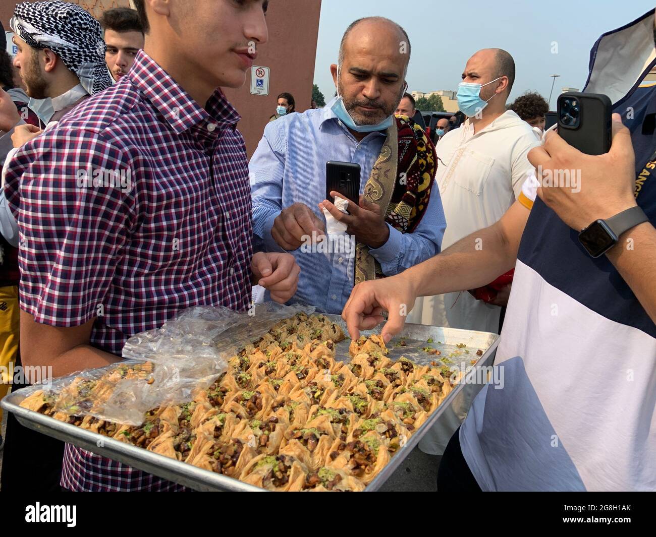Men having Arabic sweets as a crowd Muslim worshippers gather outdoor at the Hamilton Mountain mosque to worship and celebrate Eid festival. Stock Photo