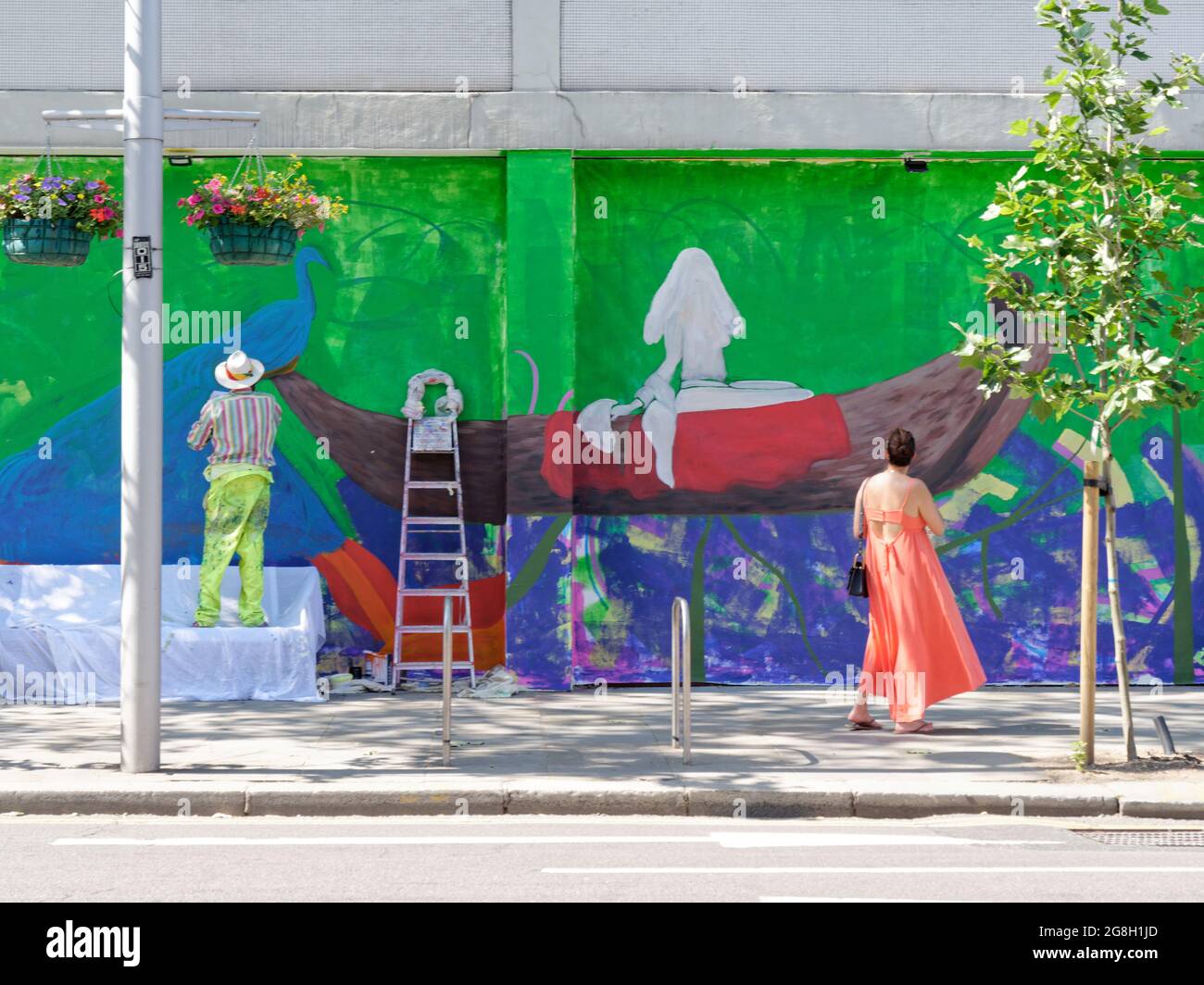 London, Greater London, England, June 12 2021: Man beside step ladder wearing paints a wall on the Kings Road as a lady observes, Chelsea. Stock Photo