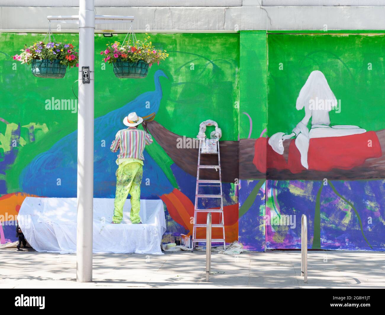 London, Greater London, England, June 12 2021: Man beside step ladder wearing a striped shirt paints a colourful wall on the Kings Road, Chelsea. Stock Photo