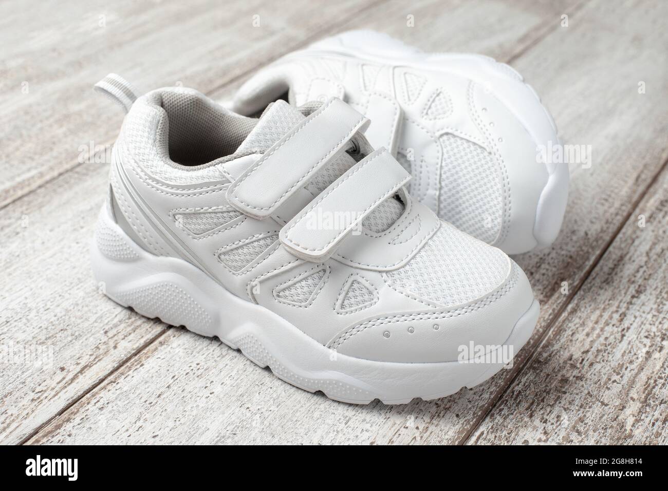 White sneakers on a light background. A pair of children's leather sports sneakers sewn with a fabric with a velcro fastener, with a shoe lying on its Stock Photo