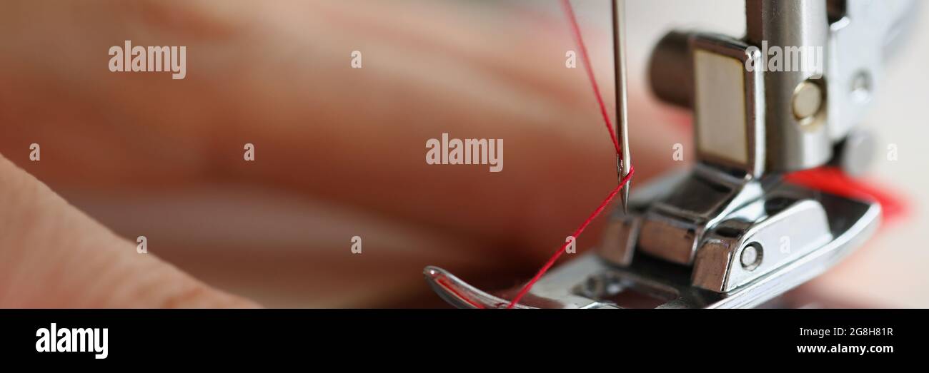 Hands pulling red thread in sewing machine needle Stock Photo