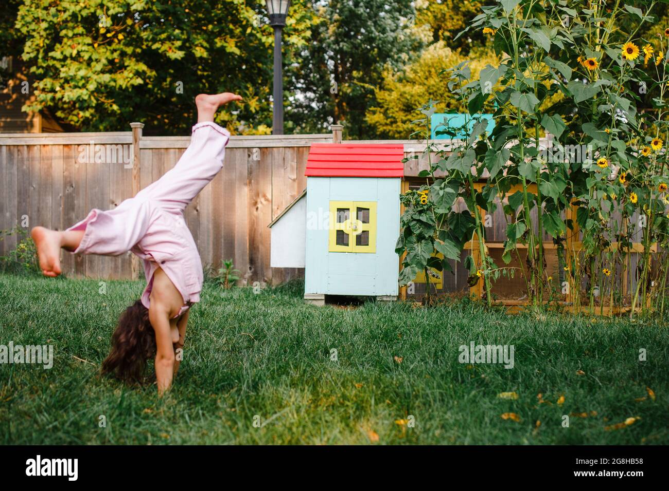 A little girl cartwheels in backyard by colorful chicken coop Stock Photo
