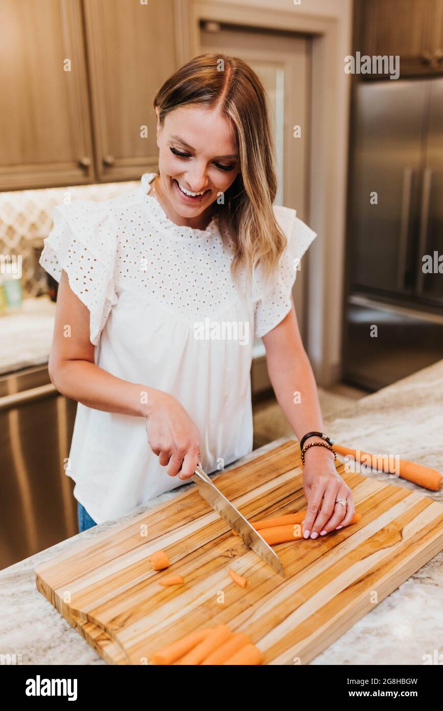 Woman chops carrots on a wooden cutting board in her kitchin Stock Photo