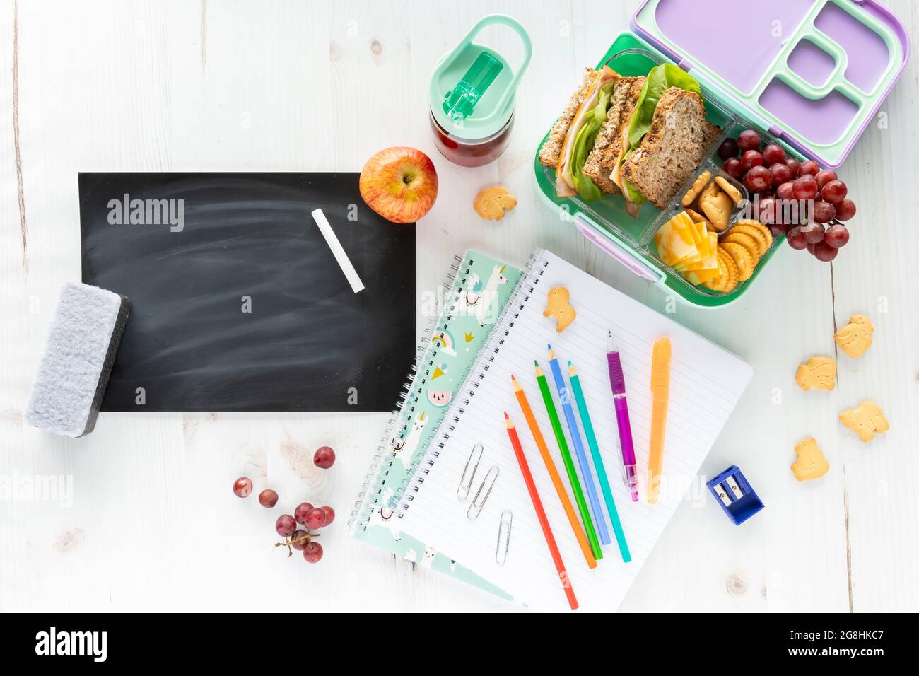 Top down view of an assortment of school supplies and lunch along with a blank chalkboard, chalk and eraser. Stock Photo