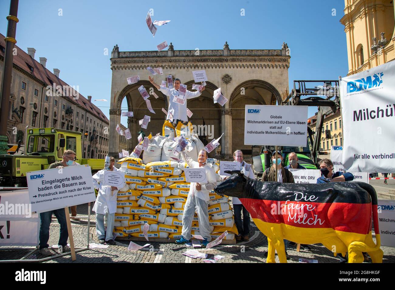 Demonstrant voller Geld, der die Macht der Milch Konzerne symbolisiert mit einem sarkastischen Schild: ' Billige Milch abholen & mit staatlichen Zuschuss einlagern. Für uns Win-Win! ' und wirft mit Geld um sich. Er steht auf 300 Säcke mit Milchpulver und Demonstranten mit Schilder und einer Milchkuh in Deutschlandfarben 'Die faire Milch'. Am 18. Mai 2020 haben zahlreiche Milchbauern für einen Milchpreis von mindest 40 Cent demonstriert. Durch die Corona Krise ist Milchpreis global deutlich gefallen und der BDM fordert einen staatlichen Eingriff. München, 18. Mai 2020. (Photo by Alexander Pohl/ Stock Photo