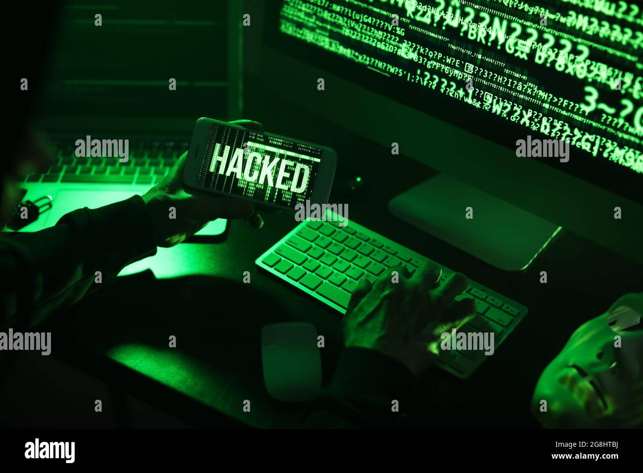 Hacker with mobile phone using computer in dark room Stock Photo - Alamy