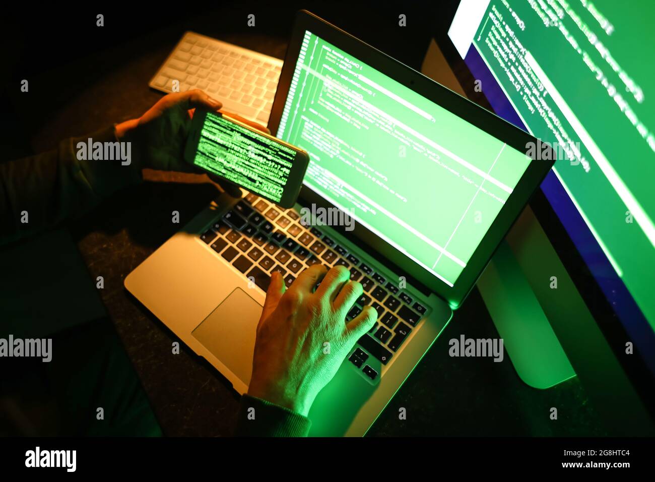 Hacker with mobile phone using computer in dark room Stock Photo - Alamy