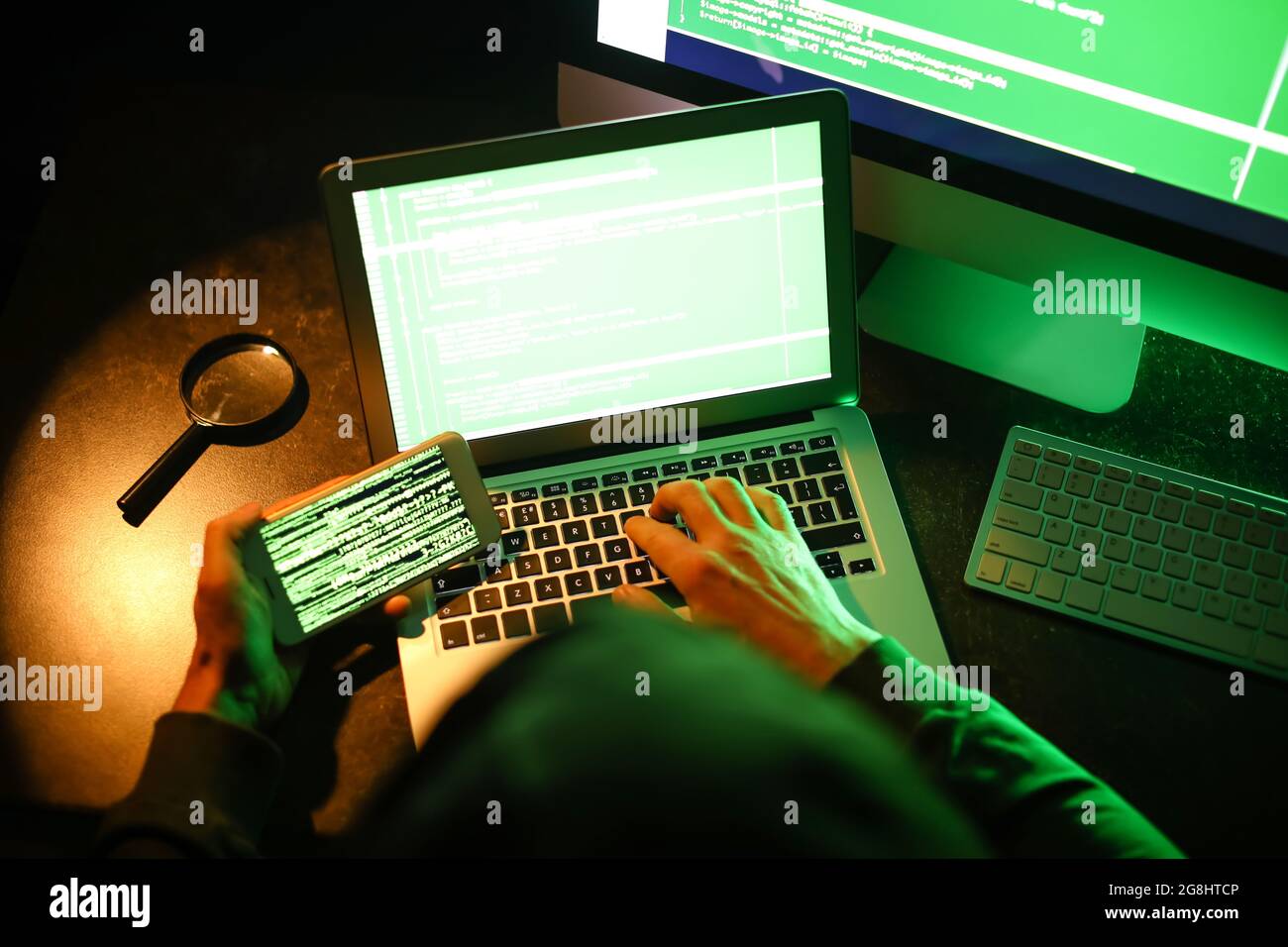 Hacker with mobile phone using computer in dark room Stock Photo - Alamy
