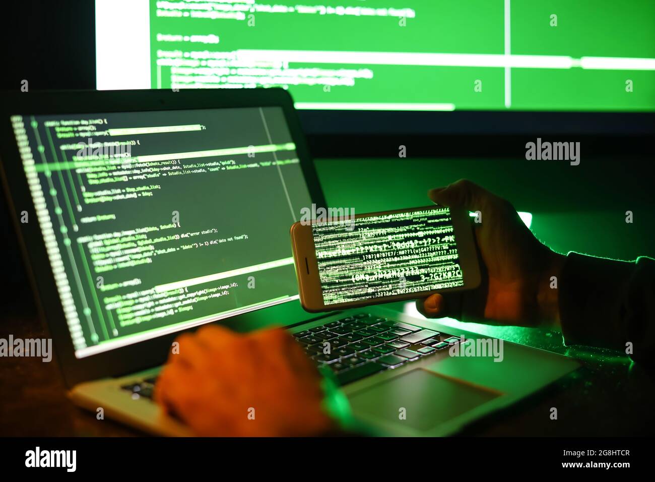 Hacker with mobile phone using computer in dark room Stock Photo - Alamy