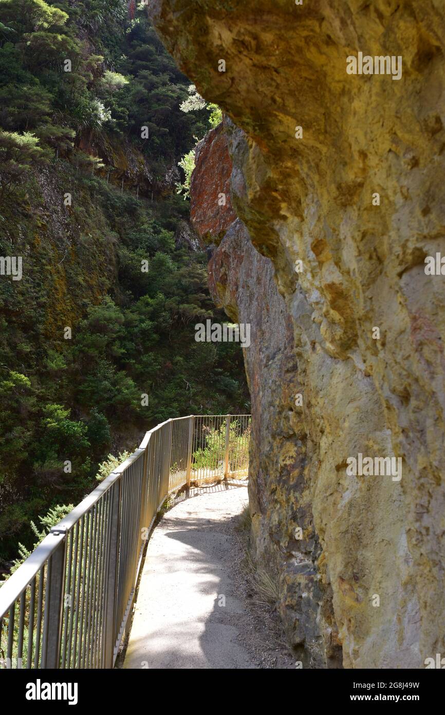 Narrow footpath with steel railing along vertical rock wall with other side of gorge in background. Stock Photo