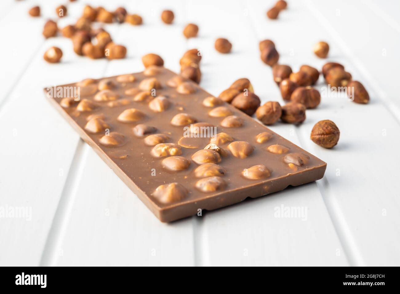 Chocolate bar with hazelnuts on white table. Stock Photo