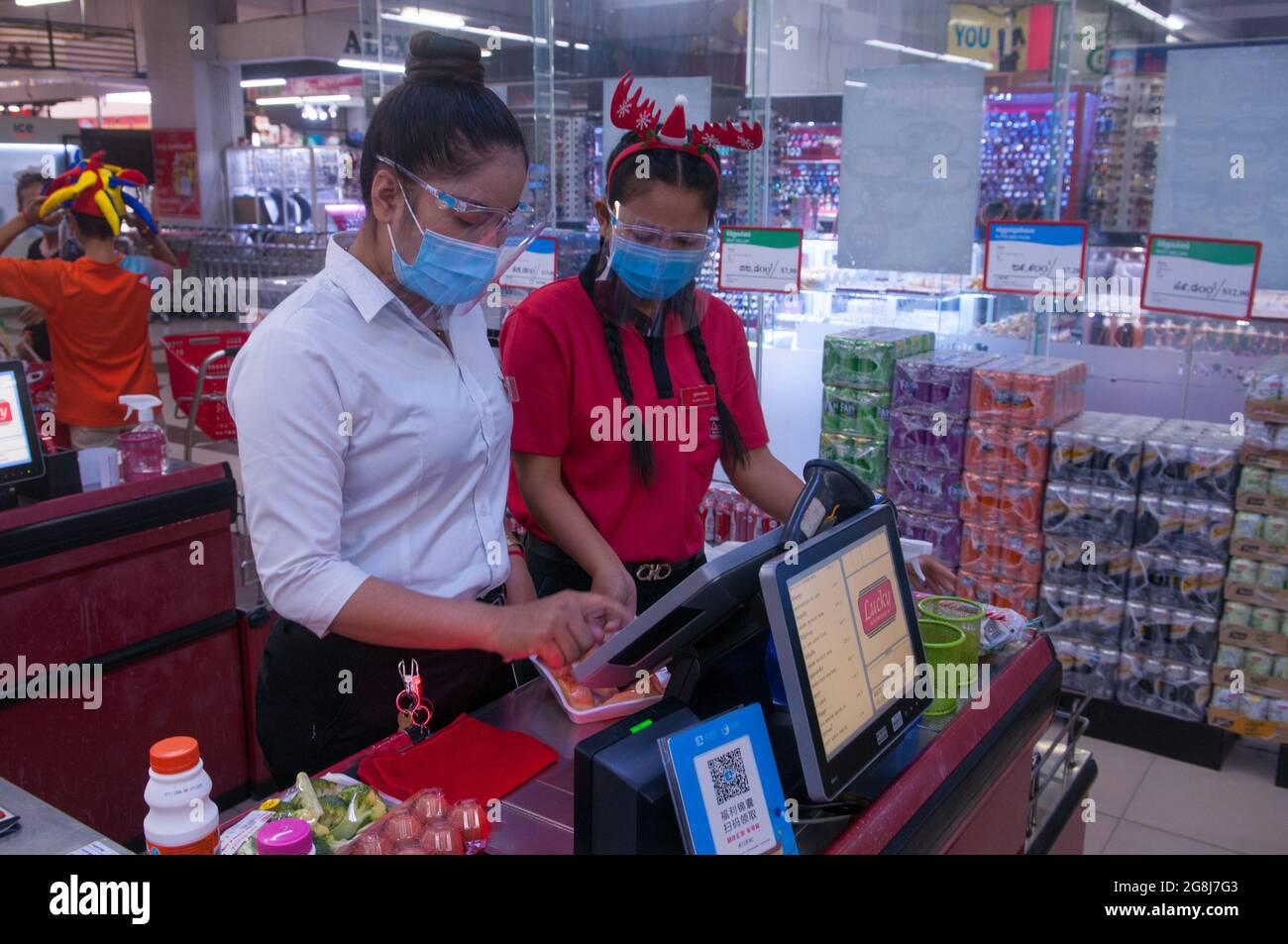 during the Christmas holidays with an outbreak of COVID - 19, two Cambodian female cashiers, wearing protective plastic face shields & masks, scan groceries at a grocery store checkout counter during the coronavirus pandemic. Steung Meanchey, Phnom Penh, Cambodia. Dec. 23rd, 2020. © Kraig Lieb Stock Photo
