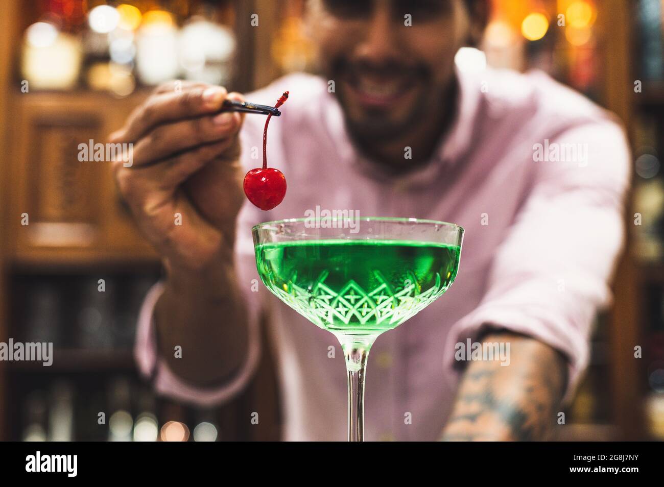 Young barman placing a cherry in a green cocktail, night party concept. Stock Photo