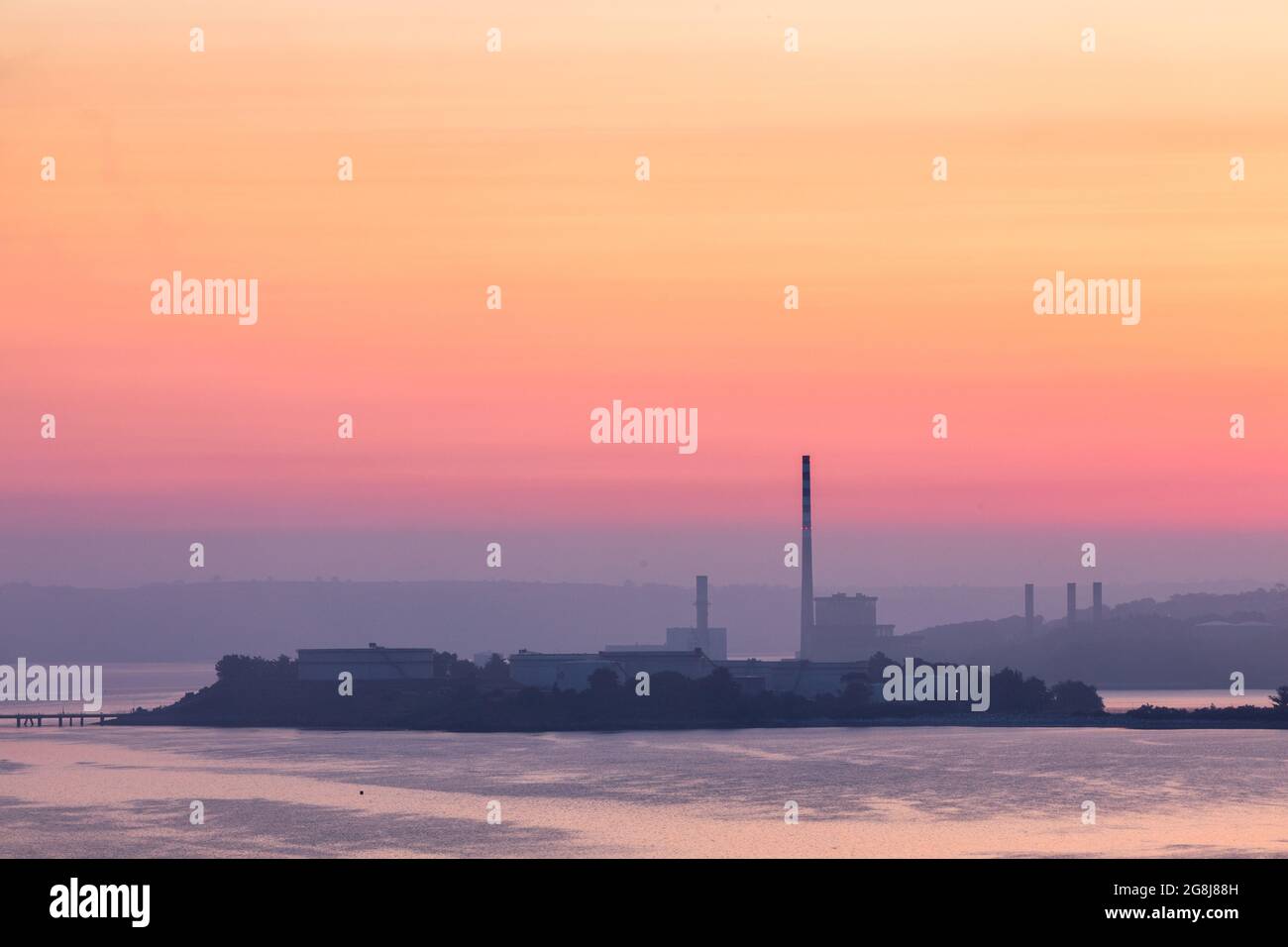 Aghada, Cork, Ireland. 21st July, 2021. With a status yellow heat warning in place an orange sky give a dramatic scene as dawn breaks over the ESB generating station in Aghada, Co. Cork, Ireland- Picture; David Creedon / Alamy Live News Stock Photo