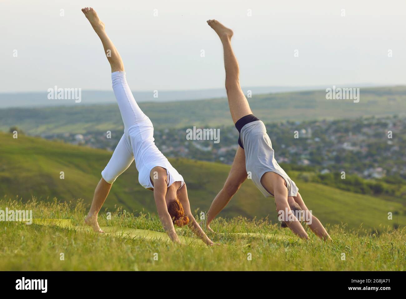 Man and woman doing One-Legged Down Dog asana together while practicing yoga in nature Stock Photo